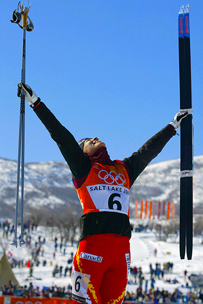 Beckie Scott in skiing attire at the Salt Lake olympics, raising her arms in triumph following her win.