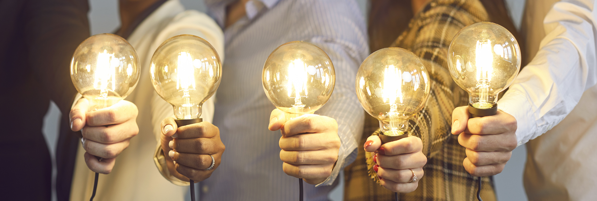 5 hands holding lit lightbulbs